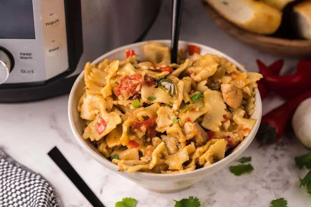 A bowl of creamy pasta with vegetables and herbs, placed on a marble surface beside an electric cooker and slices of bread&mdash;perfect for those who love easy instant pot dishes.