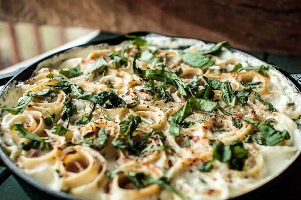 A close-up of a baked pasta dish in a skillet, topped with creamy white sauce, fresh spinach, and herbs&mdash;perfect for those seeking delicious quick pasta recipes.