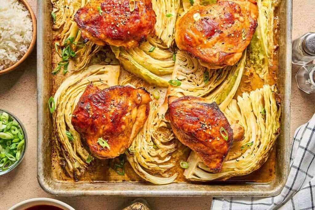 Sheet pan with roasted chicken thighs and cabbage wedges, garnished with chopped green onions&mdash;an easy nod to Asian-inspired dishes&mdash;served alongside a bowl of rice and extra sliced green onions.