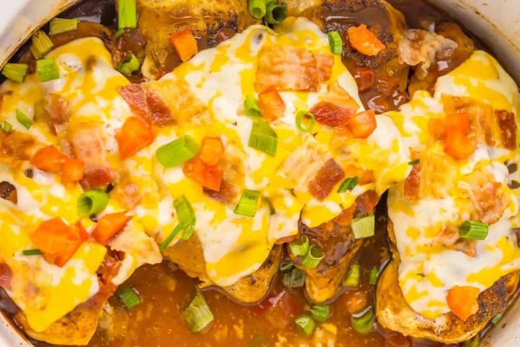 Chicken breasts covered with melted cheese, chopped bacon, diced tomatoes, and sliced green onions in a brown sauce.