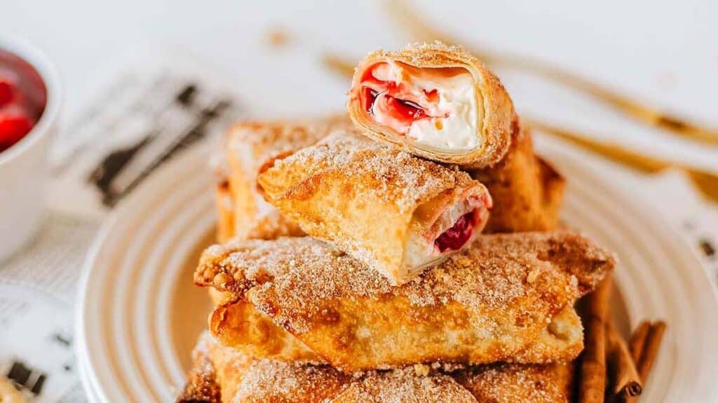 A plate stacked with cinnamon sugar-coated pastry rolls, some cut open to reveal a creamy filling with red fruit.