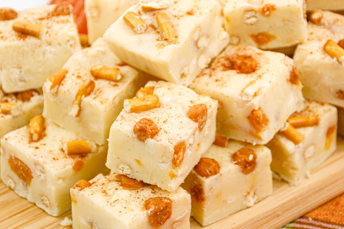A stack of white chocolate fudge squares with pretzel pieces and caramel bits on a wooden board.