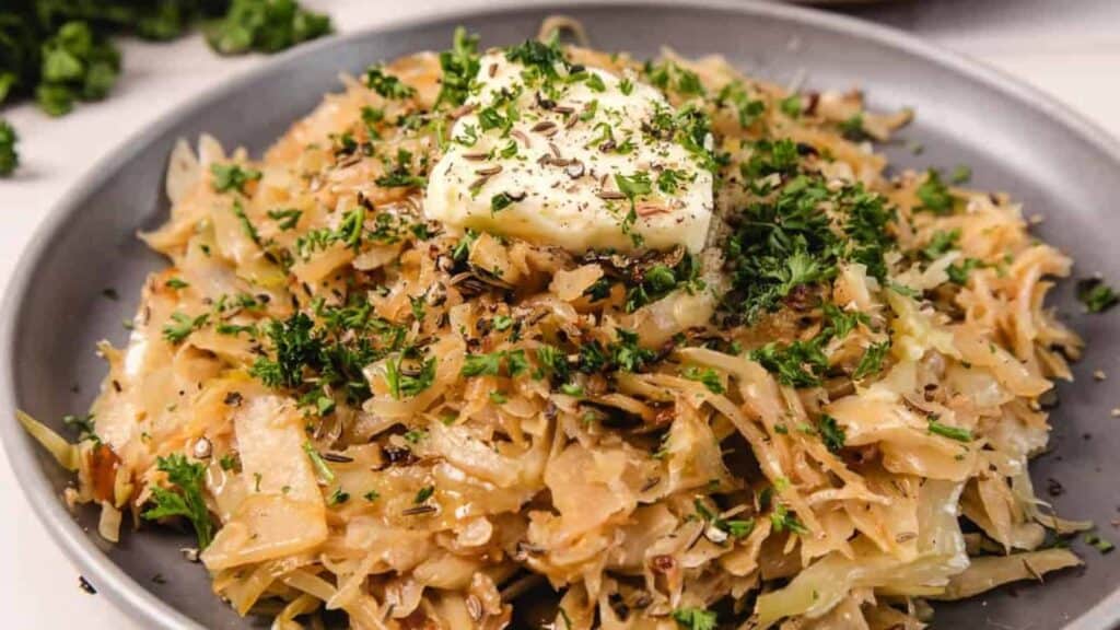 A plate of saut&eacute;ed cabbage topped with a dollop of butter and garnished with chopped parsley and herbs.
