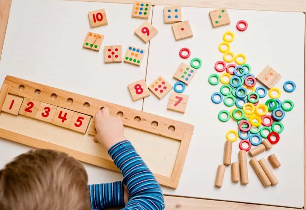 A child arranges numbered wooden tiles on a board, celebrating Pi Day with colorful rings, rods, and additional numbered tiles scattered on the table.