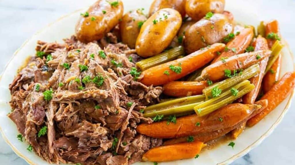 Plate with shredded pot roast, whole baby potatoes, carrots, and celery, garnished with chopped parsley.