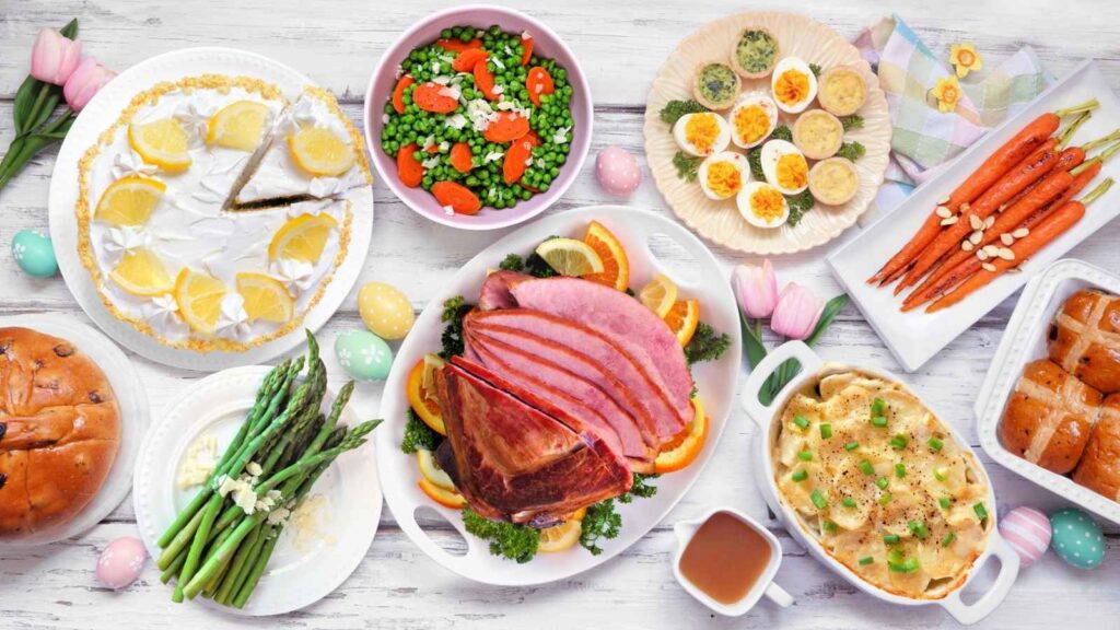 Table set with ham, lemon pie, bread, deviled eggs, peas and carrots, glazed carrots, asparagus, and a baked casserole, arranged for a meal.