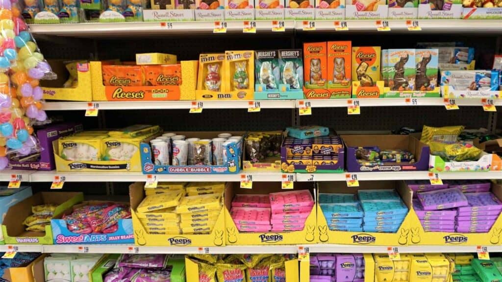 Shelves stocked with various Easter candies, including Peeps, Reese's, M&M's, chocolate bunnies, and other colorful packaged sweets.