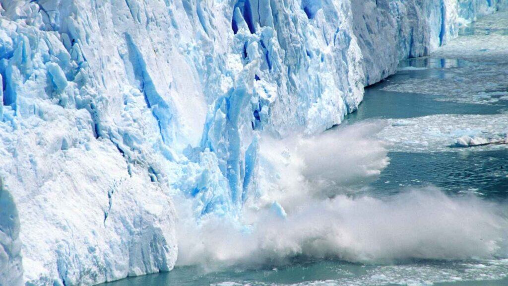 Large chunks of ice break off a glacier and fall into the water, creating splashes and waves.