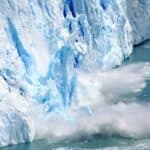 Large chunks of ice break off a glacier and fall into the water, creating splashes and waves.
