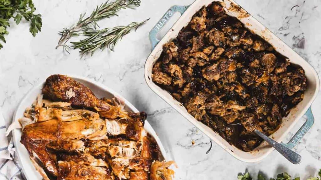 Two dishes on a marble surface: one with shredded roasted turkey, the other with dark stuffing or cooked meat, garnished with fresh herbs.
