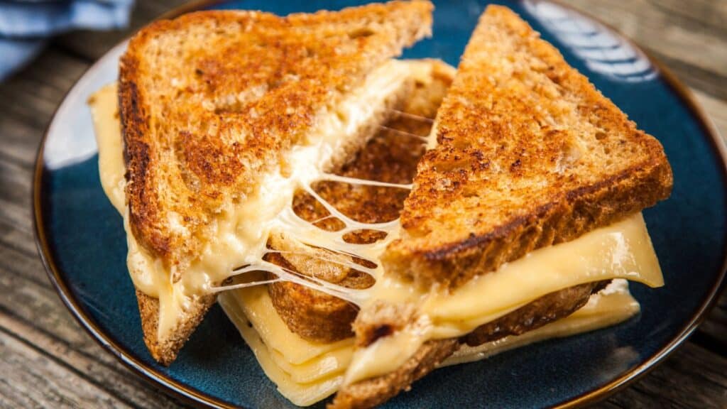 A grilled cheese sandwich cut in half on a plate, with melted cheese stretching between the slices of toasted bread.