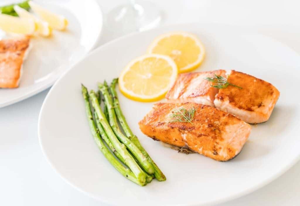 Two pieces of cooked salmon with asparagus spears and lemon slices on a white plate.