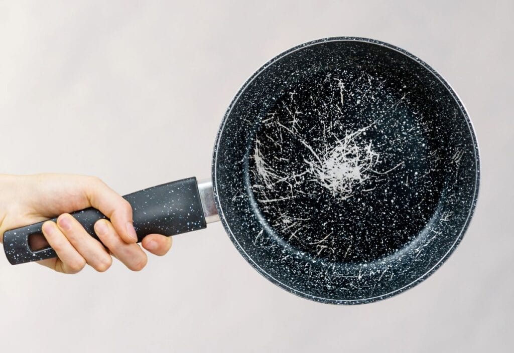 A hand holding a scratched and worn nonstick frying pan against a plain background.