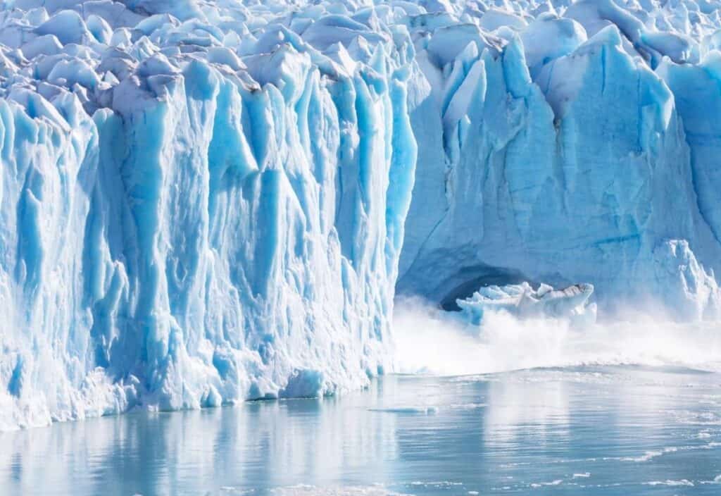 A large section of blue glacier ice breaks off and falls into the water, creating a splash and mist at the base of the glacier&mdash;an awe-inspiring sight fitting for World Day of Glaciers.