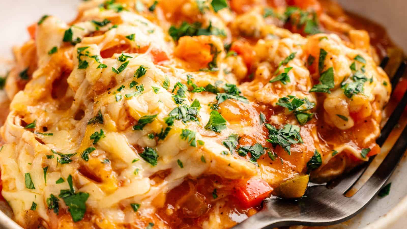 Close-up of a cheesy, baked casserole topped with chopped parsley and diced vegetables, being served with a metal spatula.