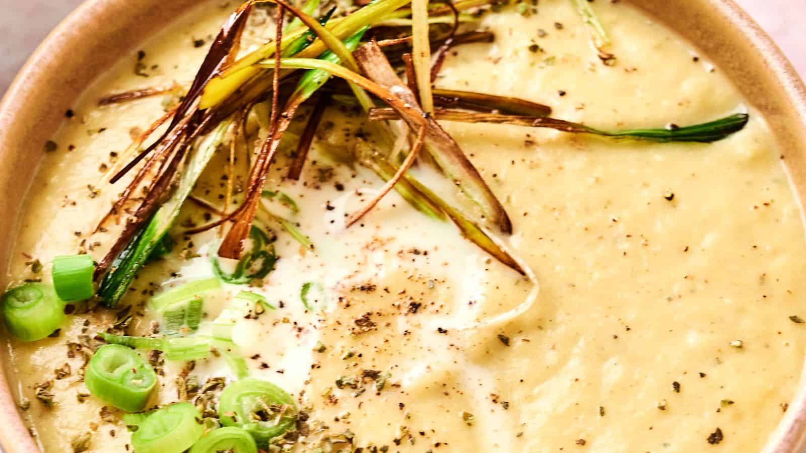 A bowl of creamy soup topped with sliced green onions, crispy fried leeks, cracked black pepper, and herbs.