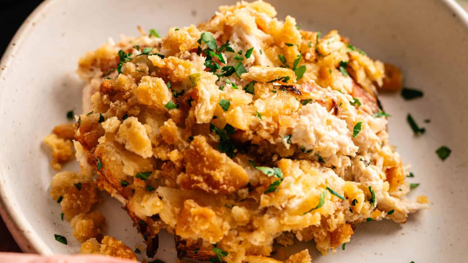 A serving of chicken and stuffing casserole garnished with chopped parsley on a beige plate.