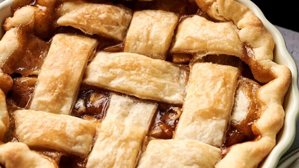 Close-up of a baked pie with a golden brown lattice crust, showing the filling beneath the woven pastry strips.