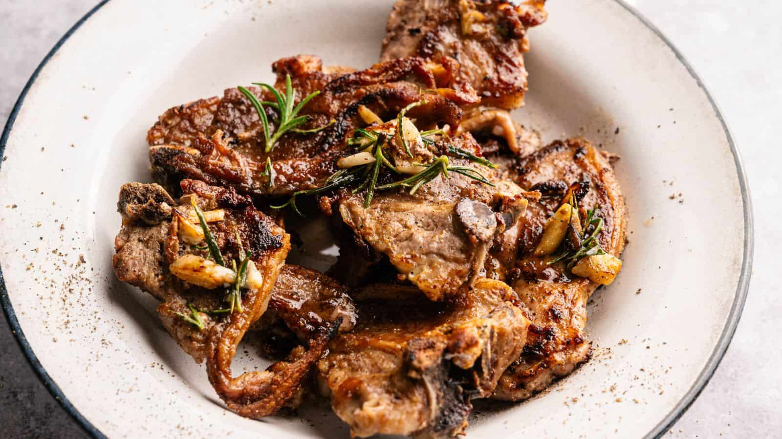 Grilled lamb chops garnished with rosemary and garlic, served on a white plate.