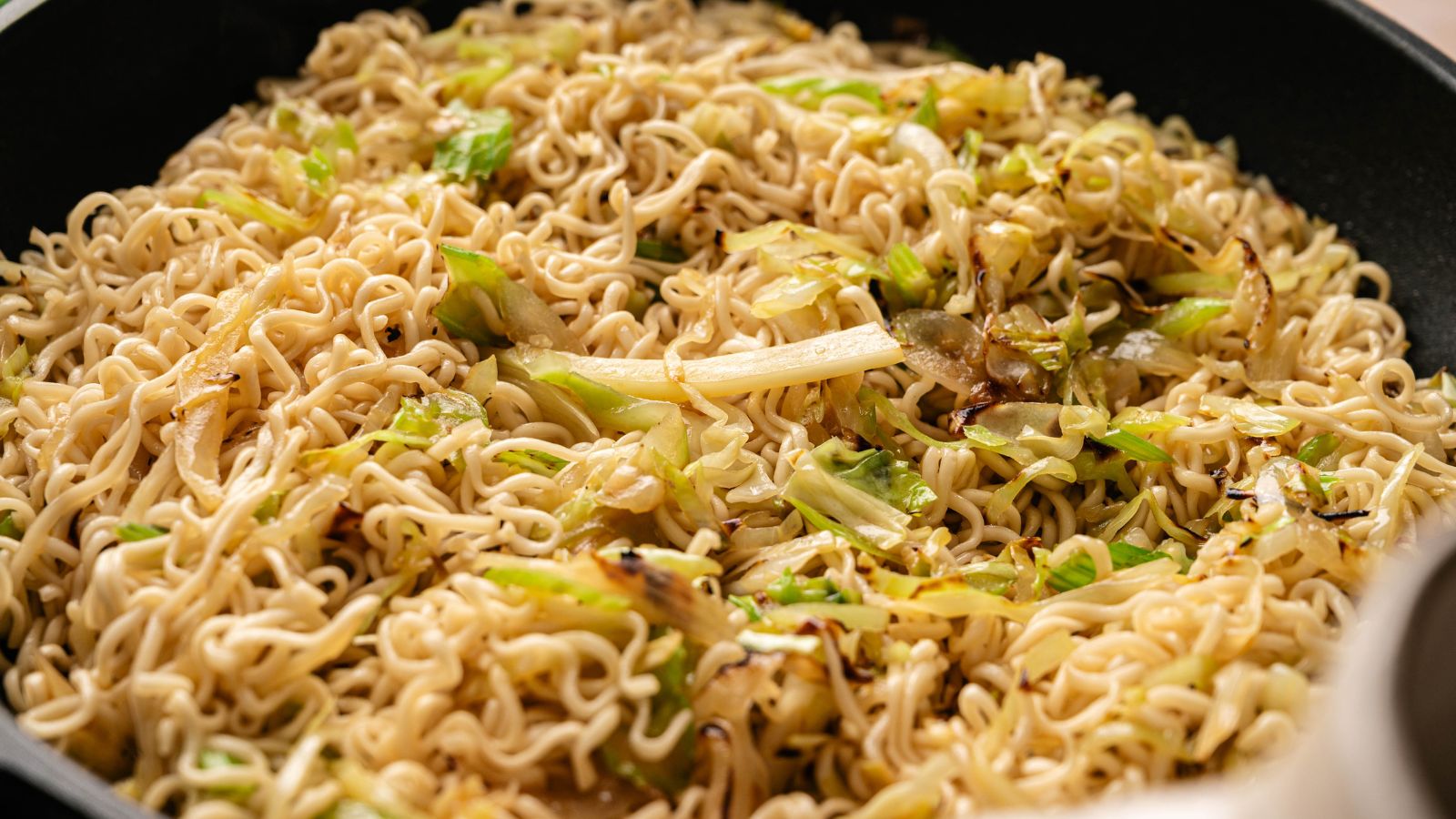 A close-up of cooked instant noodles mixed with saut&eacute;ed cabbage and onions in a pan.