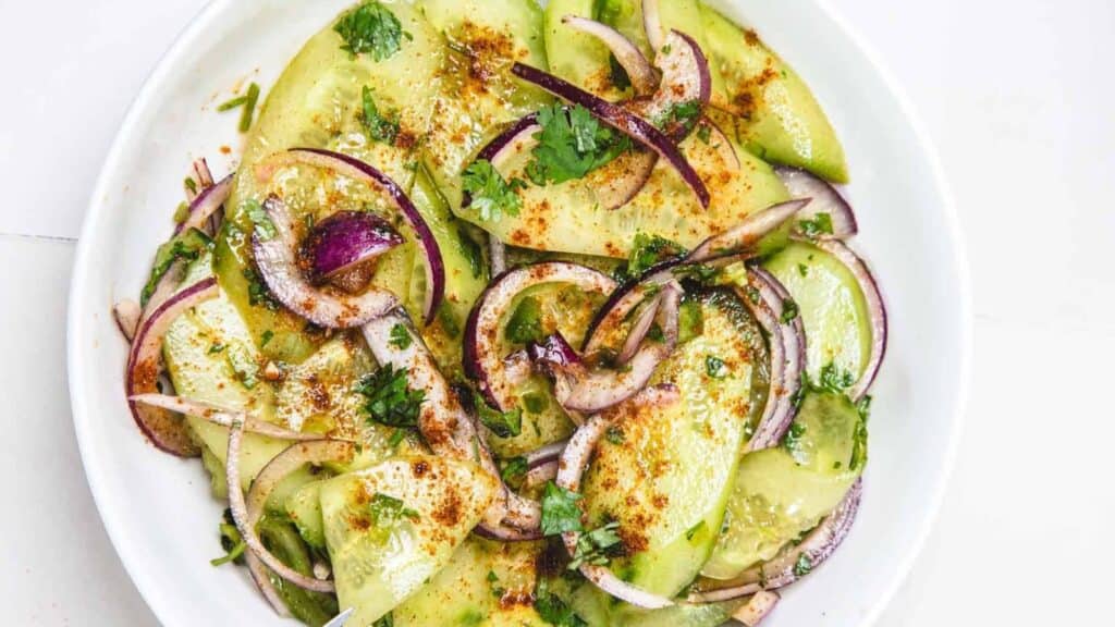 Sliced avocado and red onion topped with cilantro, spices, and a light dressing served on a white plate.