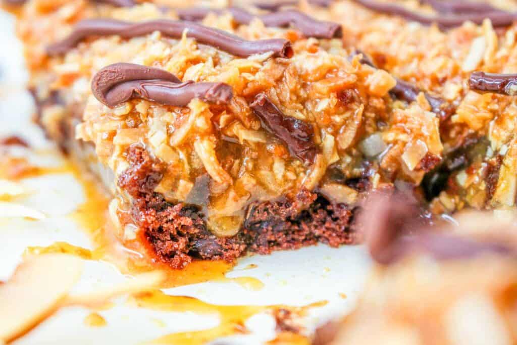 Close-up of a dessert bar with a chocolate base, topped with caramelized coconut and drizzled chocolate.