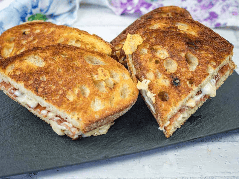 Four grilled cheese sandwiches with hot honey butter on a black slate serving board.