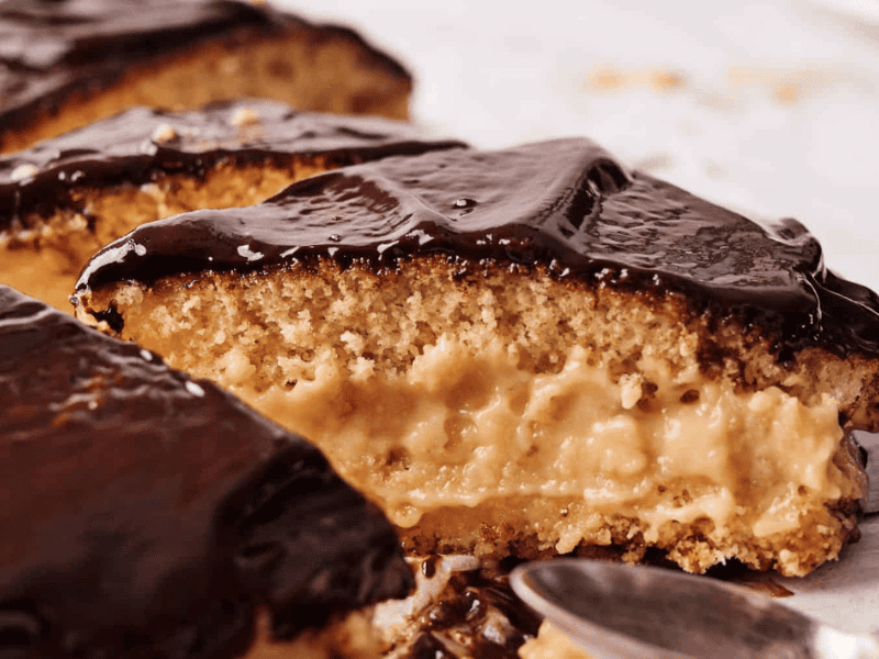 A close-up of sliced Boston cream pie showing yellow sponge cake layers filled with creamy custard and topped with glossy chocolate glaze.