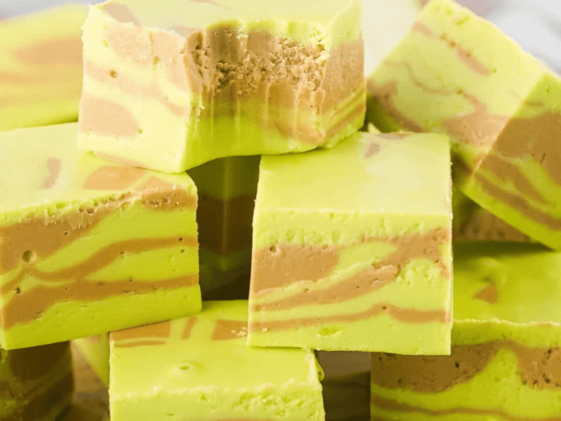 A stack of green and brown swirled fudge cubes. The top cube has a bite taken out of it.