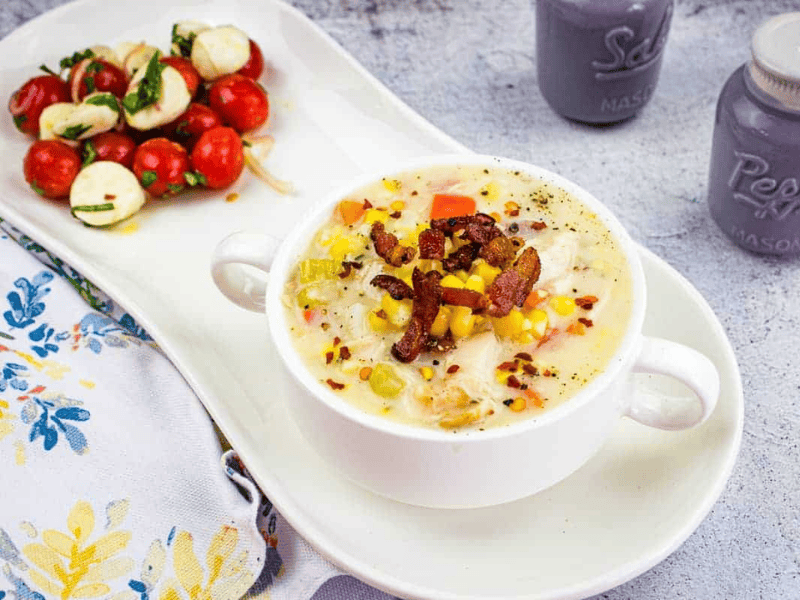 Chicken & Corn Chowder in a black bowl, topped with bacon, scallions, and red pepper flakes.