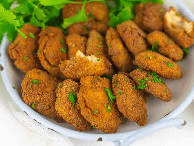 Three bowls filled with golden-brown chicken nuggets garnished with chopped parsley, served with a small bowl of creamy dipping sauce.