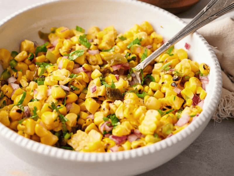 A bowl of freshly made Copycat Chipotle corn salsa with a serving spoon in it.