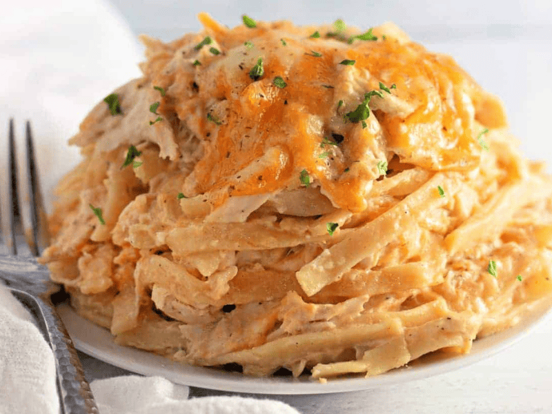 A plate of Chicken Tetrazzini topped with melted cheese and sprinkled with chopped herbs, with a fork and napkin beside it.