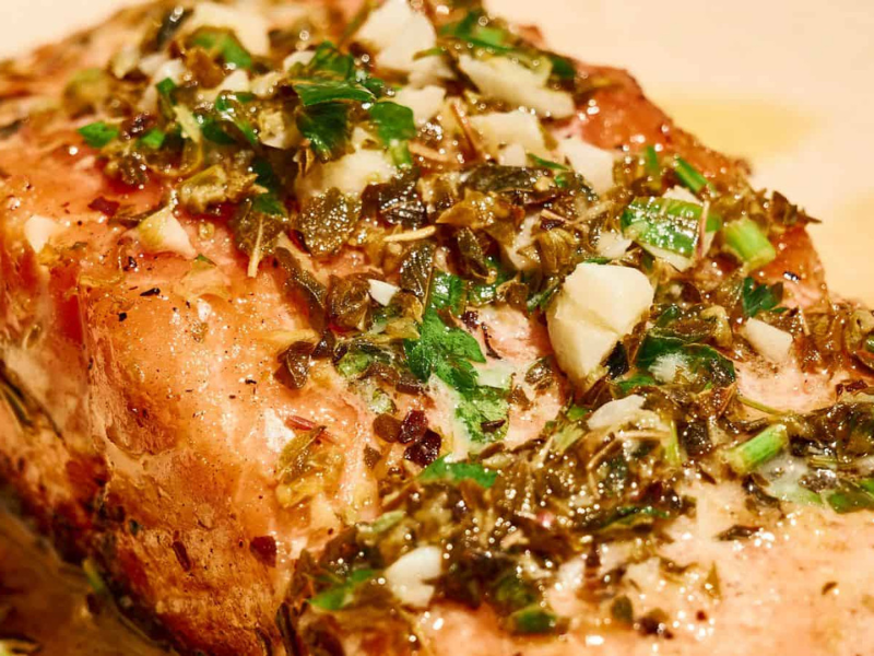 A close-up of a cooked salmon fillet topped with a mixture of chopped herbs, garlic, and seasonings.