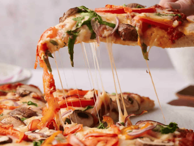 Someone taking a slice of veggie pizza.