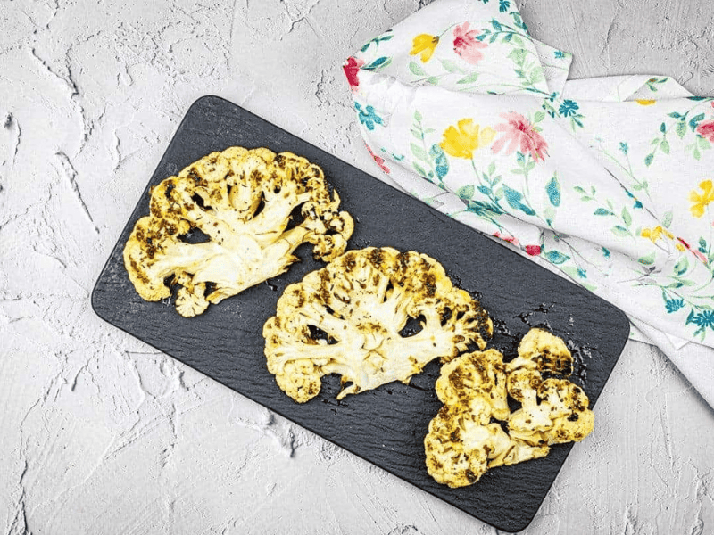 Three pieces of grilled cauliflower steaks on a black plate.