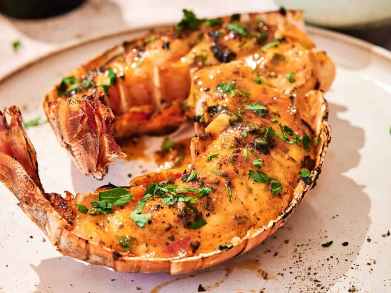 Cooked lobster tail with herbs and seasoning served on a white plate.
