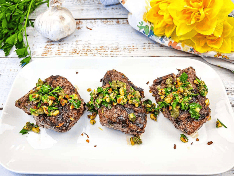 Three Grill Mediterranean Lamb Chops topped with gremolata on a white plate.