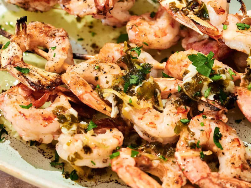 Grilled shrimp skewers served on a plate, topped with chopped herbs and a drizzle of sauce.