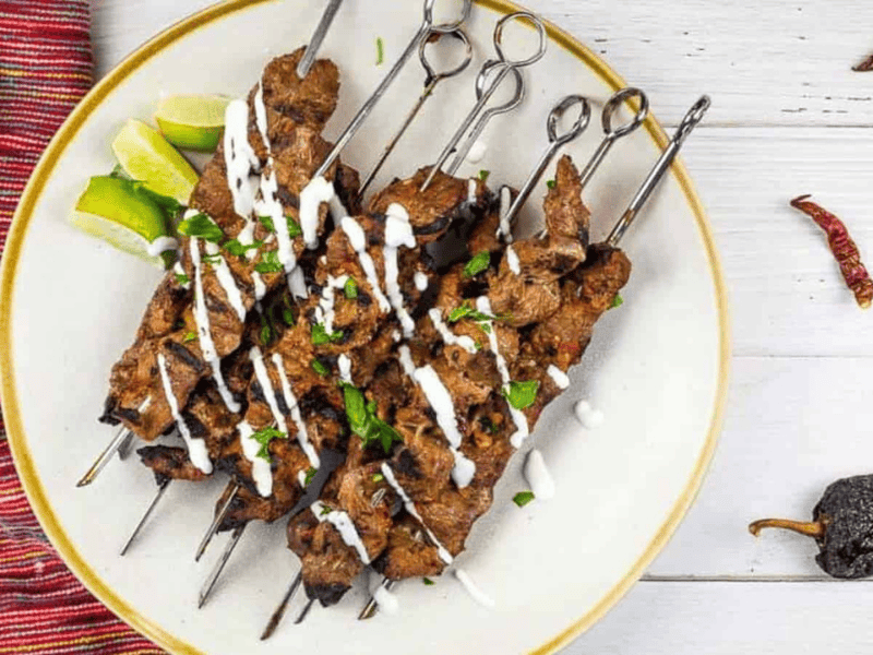 Grilled Steak skewers on a white plate with chilis nearby.