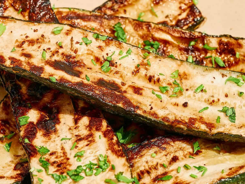 Grilled zucchini slices garnished with chopped herbs on a light-colored plate.