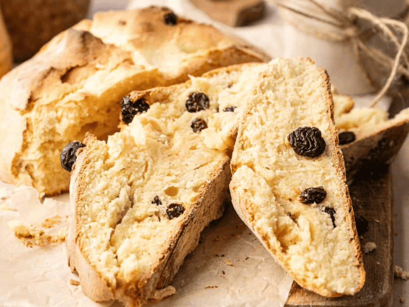 Sliced loaf of rustic bread with raisins on a wooden board and parchment paper.