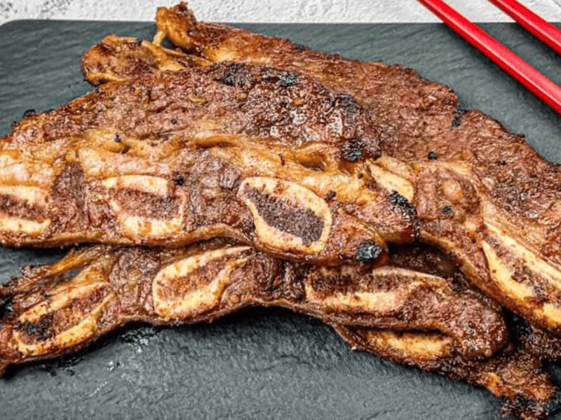 Korean Galbi Ribs on a slate platter with red chopsticks beside them.