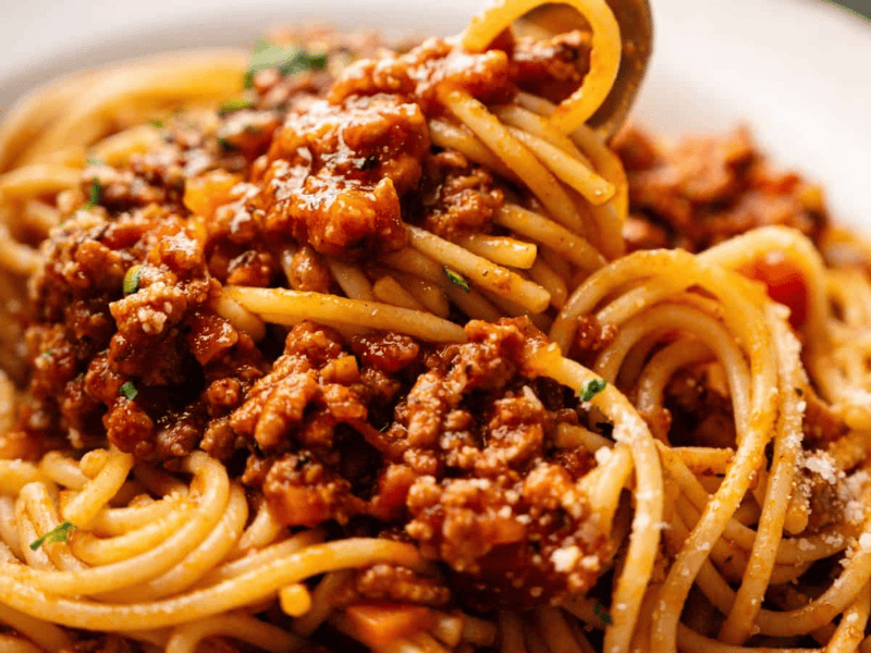 A plate of spaghetti topped with meat-based tomato sauce and grated cheese.