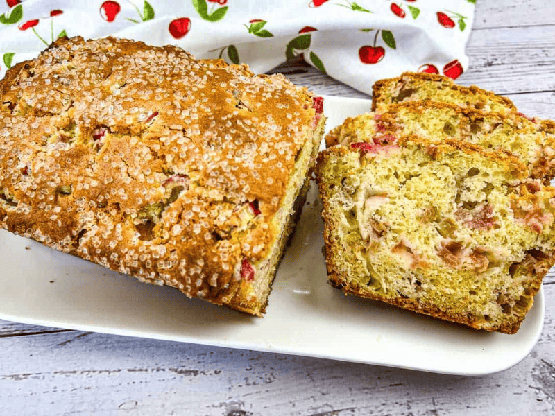 A loaf of Rhubarb Bread with a few slices on a white plate.