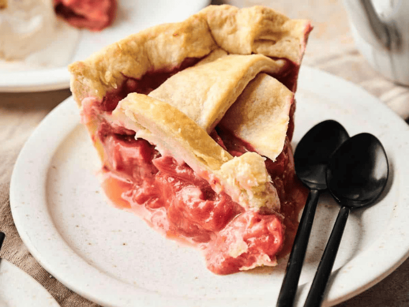 Slice of strawberry pie on a plate with two black spoons beside it.