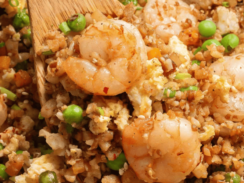 Shrimp fried rice with peas, eggs, and diced vegetables being stirred with a wooden spatula.