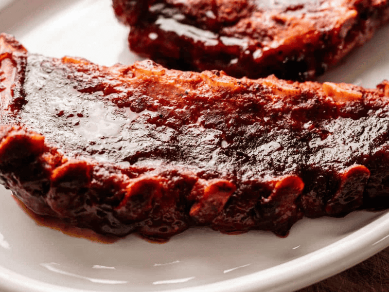 A close-up of a barbecued pork rib with a glossy layer of barbecue sauce on a white plate.