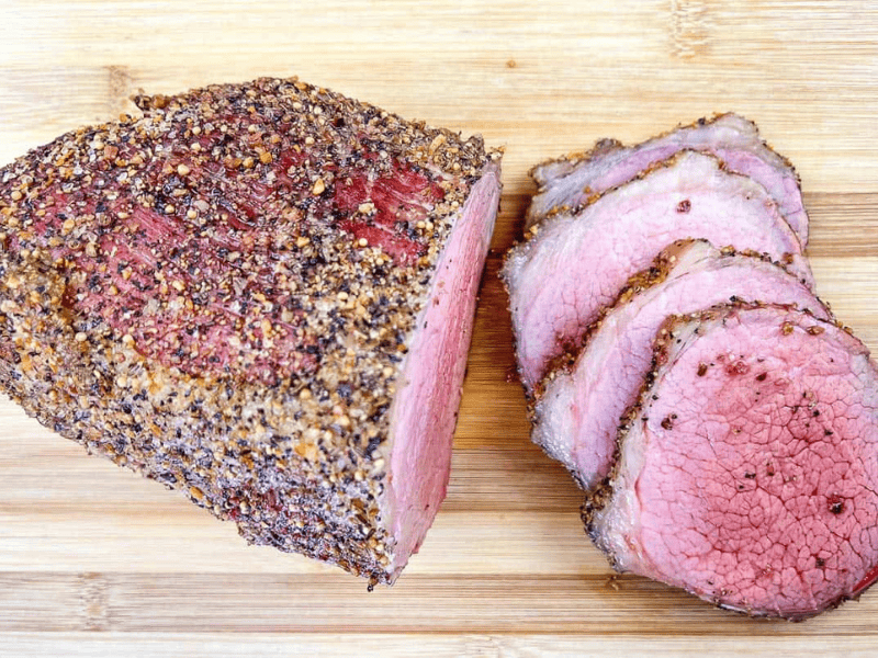 A whole and sliced smoked eye of round with on a wooden cutting board.
