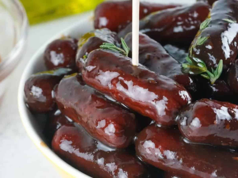 A bowl of smoked lil smokies with sauce and dipping sauce.